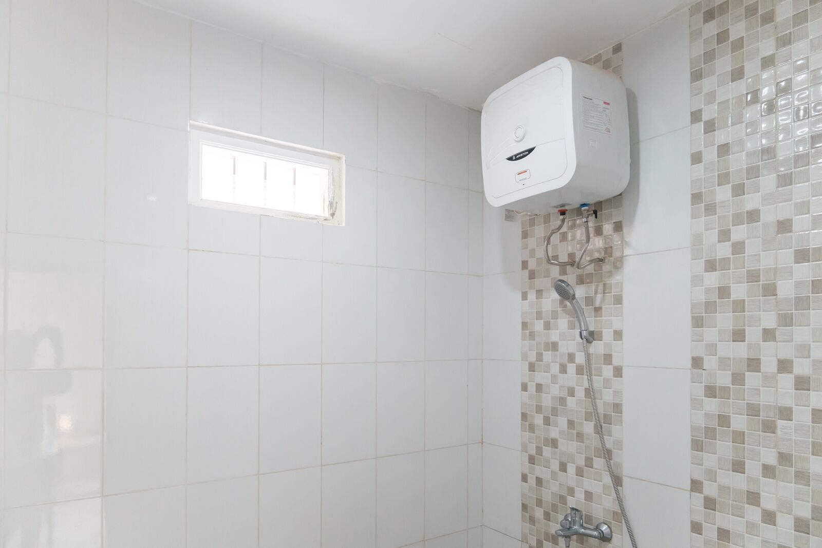 A bathroom with white tiles, a shower with a tiled wall, and a window.