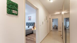 Een moderne hotelgang met een bed, een groene muur met een logo en een zithoek met stoelen en een tafel.