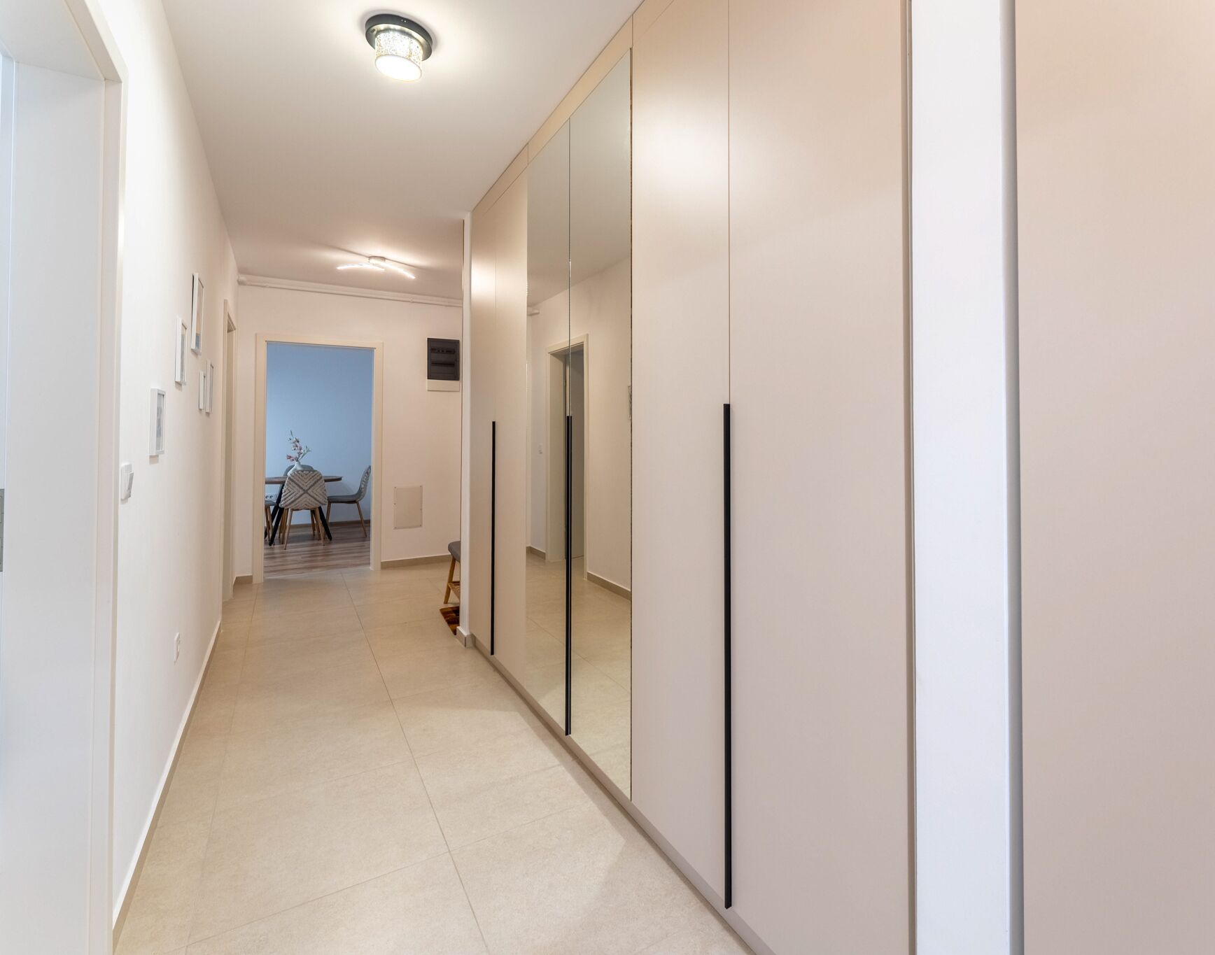 Ein moderner Flur mit einem Spiegelkleiderschrank, einem Essbereich mit Tisch und Stühlen und Blick in einen weiteren Raum.