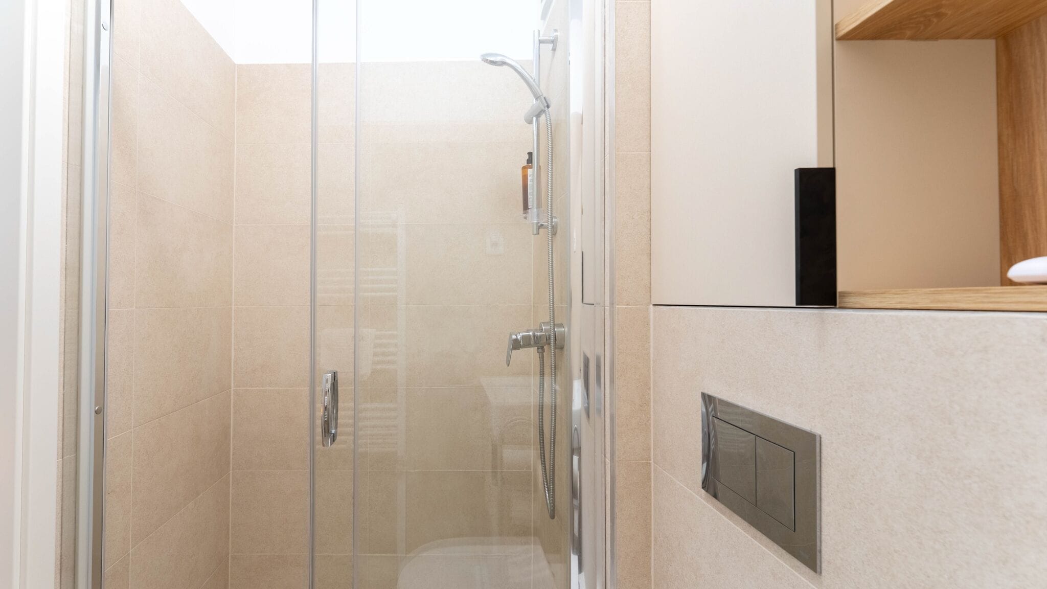 A glass-enclosed shower with a handheld showerhead and a wall-mounted faucet.