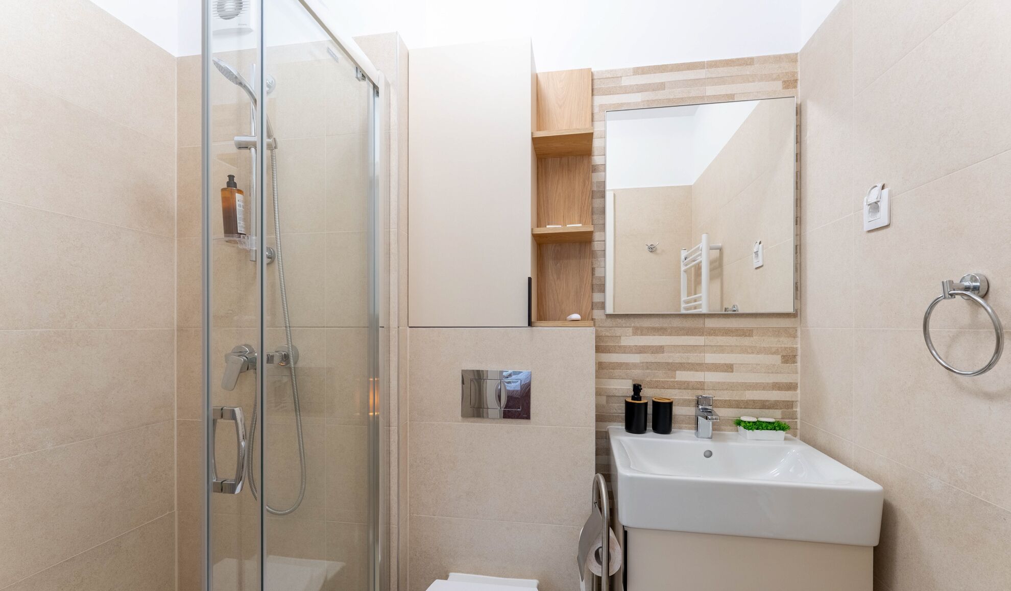 Un baño moderno con cabina de ducha de vidrio, un lavamanos con espejo y un estante de madera con artículos de aseo.