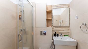 Un baño moderno con cabina de ducha de vidrio, un lavamanos con espejo y un estante de madera con artículos de aseo.