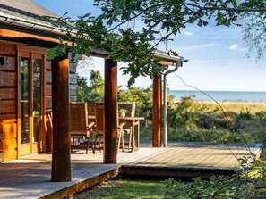 Eine Holzjagdhaushütte mit Terrasse, die auf einen Strand blickt.