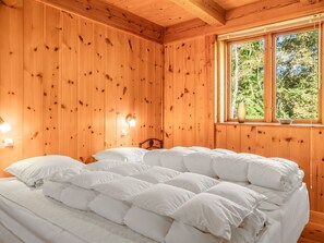 Ein Schlafzimmer einer Holzhütte mit einem Bett, einem Nachttisch und einem Fenster mit Blick auf Bäume.