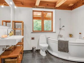 Ein modernes Badezimmer mit Holzbalkendecke, einem weißen Waschbecken, einer Toilette und einer Badewanne.