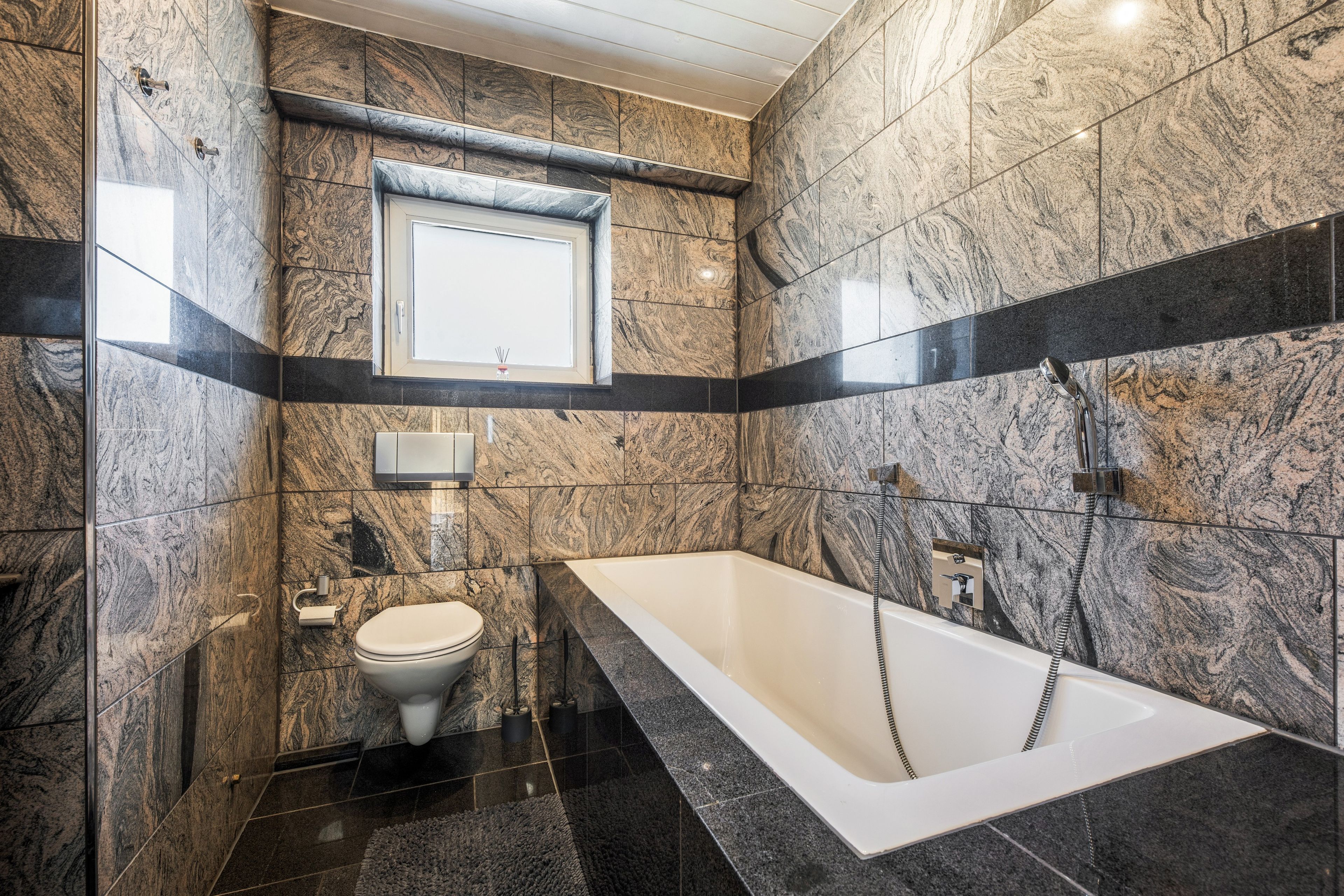 Ein modernes Badezimmer mit Badewanne, Toilette und einem Fenster über dem Waschbecken.