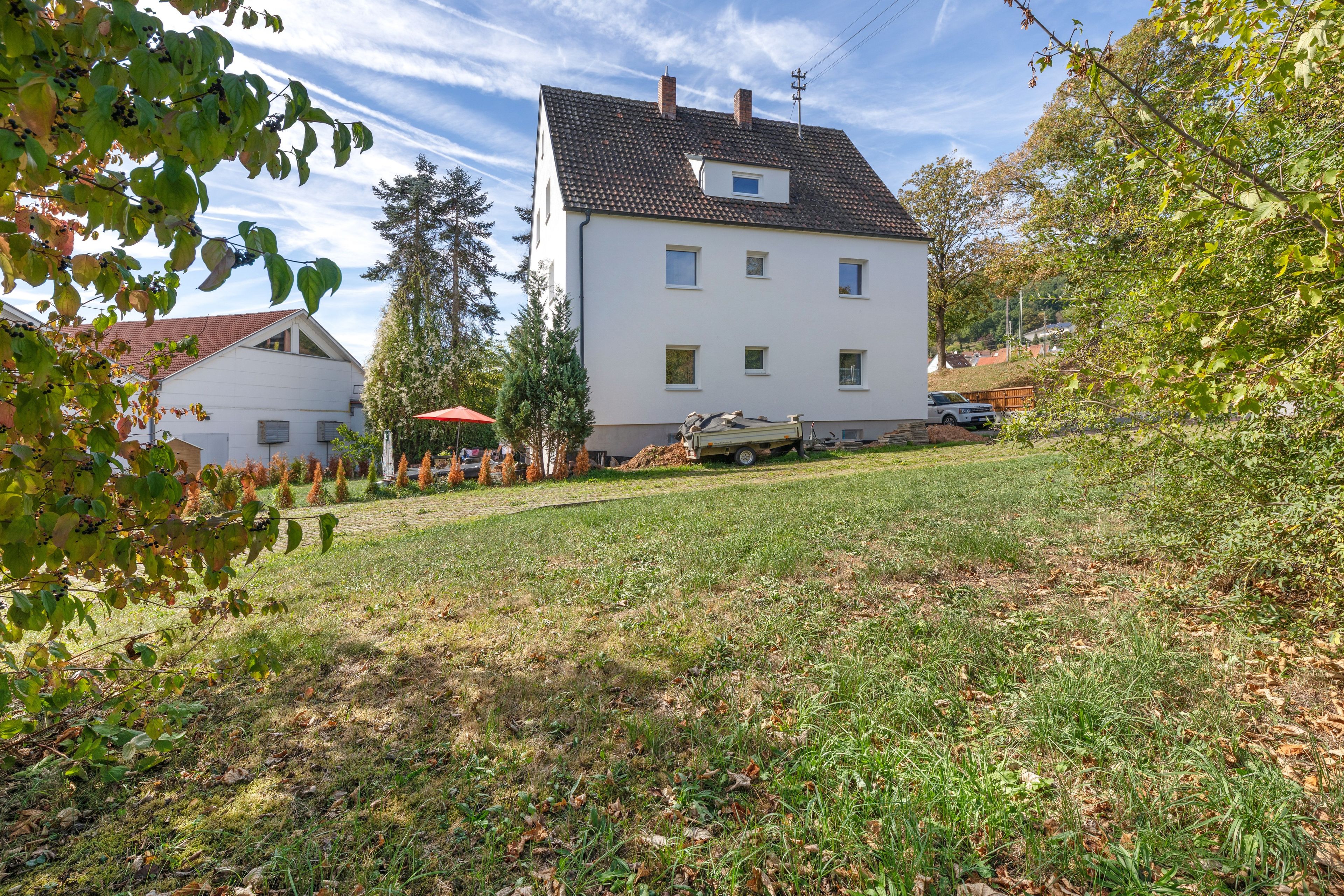 Une maison à deux étages avec un toit en pente, une petite fenêtre à l’étage supérieur et une allée pavée menant à un véhicule garé.