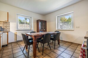 Un comedor con una mesa y sillas de madera, un mueble de almacenamiento y dos ventanas con vistas a árboles.