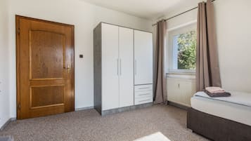 Ein Schlafzimmer mit Holztür, einem Kleiderschrank, einem Heizkörper, einem Fenster mit Vorhängen und einem Bett mit Handtüchern.