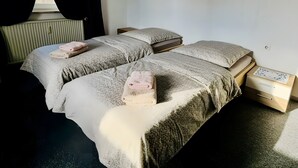 Ein Zimmer mit zwei Betten, einem Heizkörper, einem Fenster mit Vorhängen und einem Nachttisch mit einem Buch.