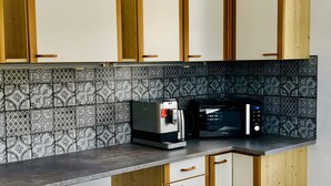 Eine Küche mit Mikrowelle, Wasserkocher und Kaffeemaschine auf der Arbeitsfläche. Ein Holztisch mit zwei Platzsets und einem Stuhl.