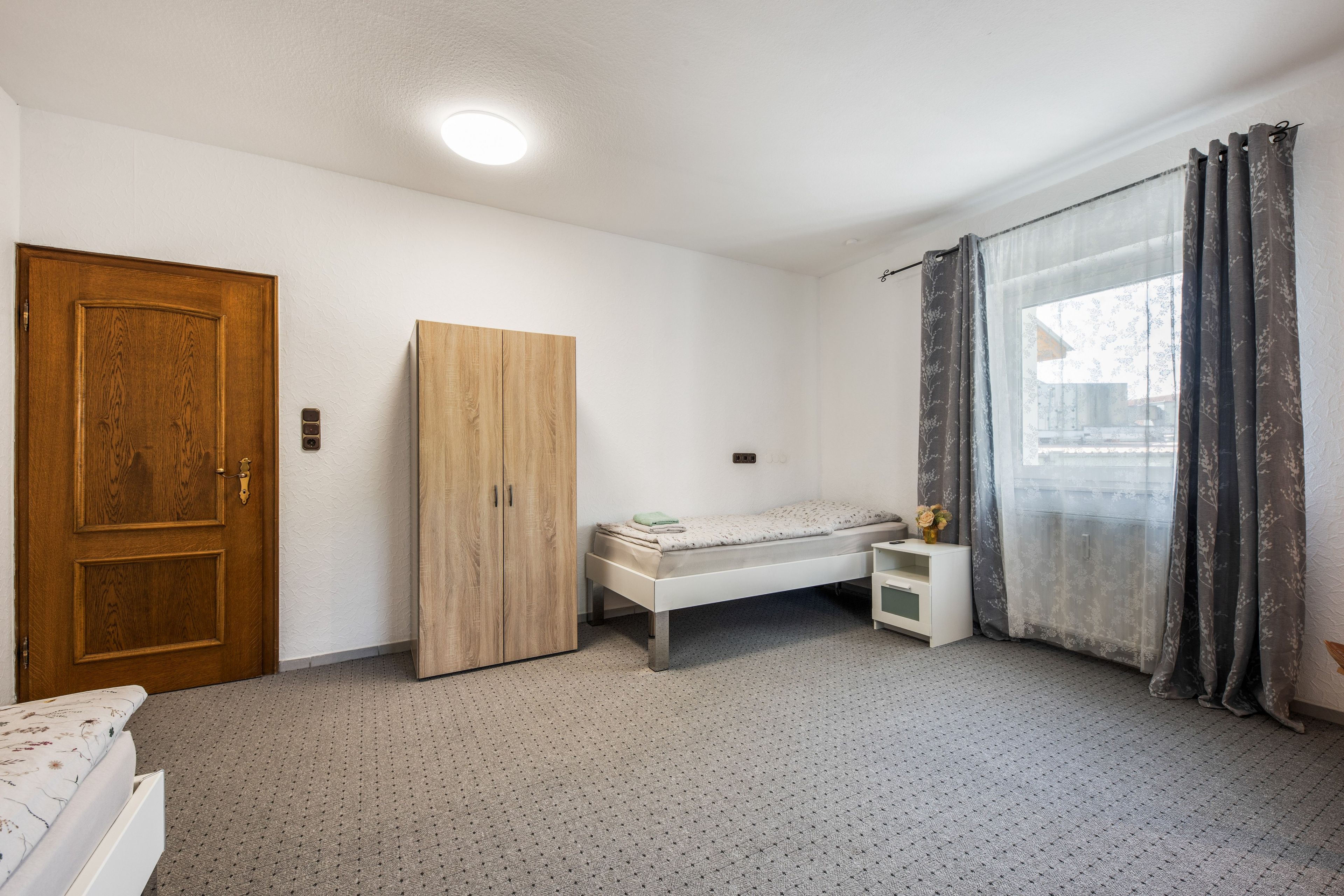 A bedroom with a bed, a wardrobe, a bedside table, and a window with curtains.