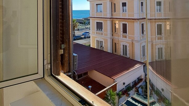 A window view of a building with a red roof, balconies, and a clear blue sky. - Sea Vibes Rome - Relax by the sea and reach Rome in minutes (Lido di Ostia)