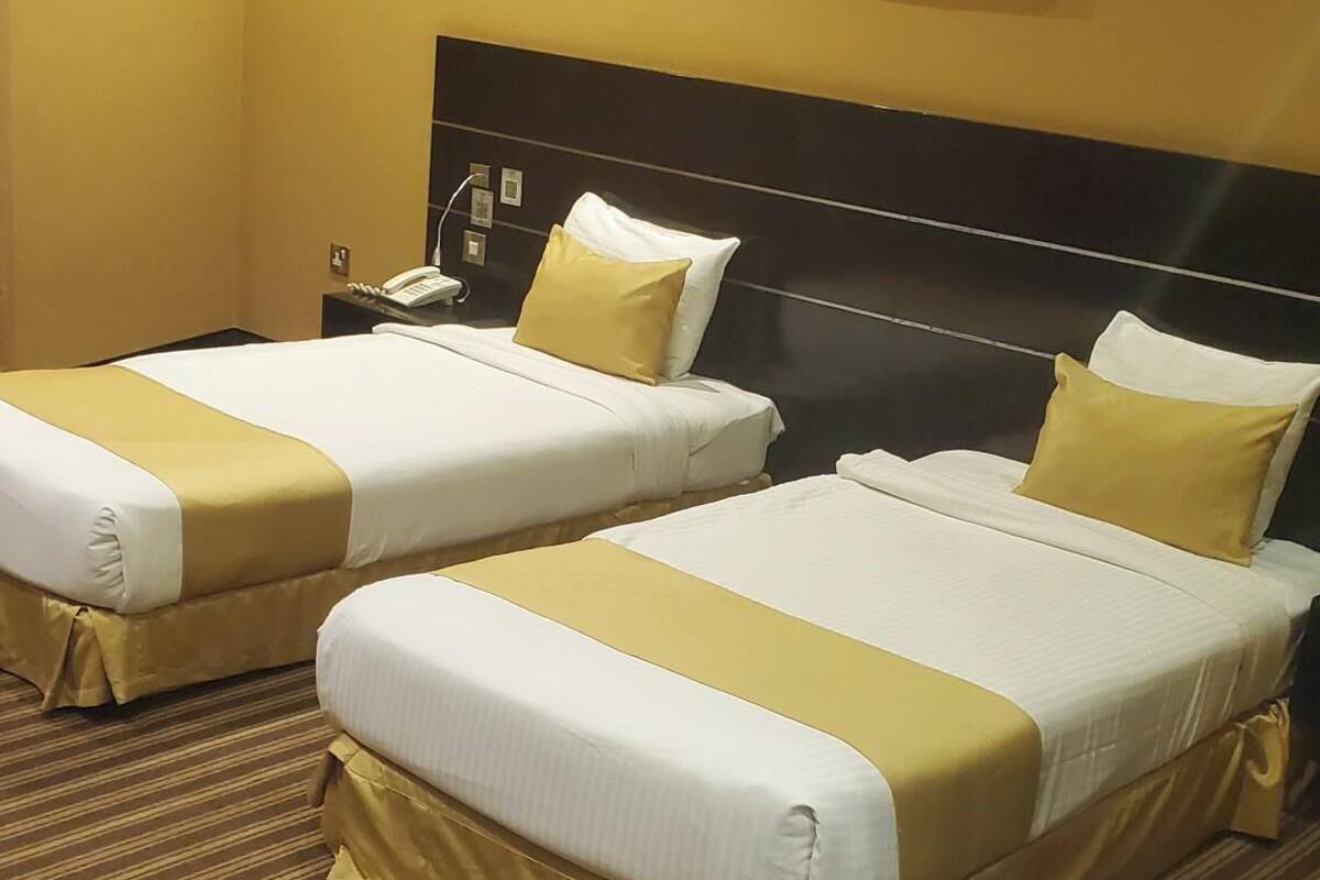 A hotel room with two beds, each with white bedding and gold accents, a headboard, a painting on the wall, and a striped carpet.