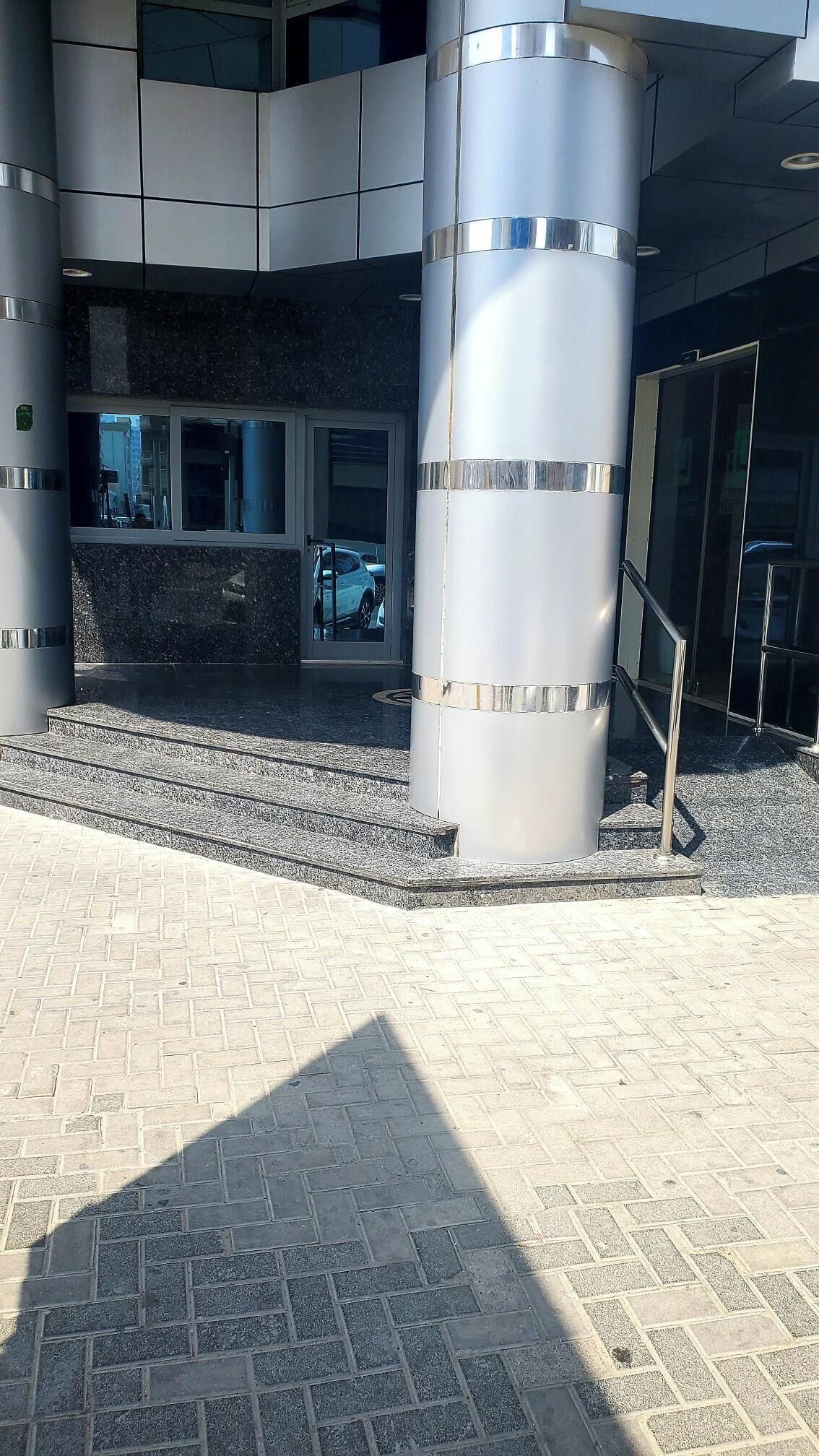 A modern building entrance with a glass door, a metal staircase, and a paved area.