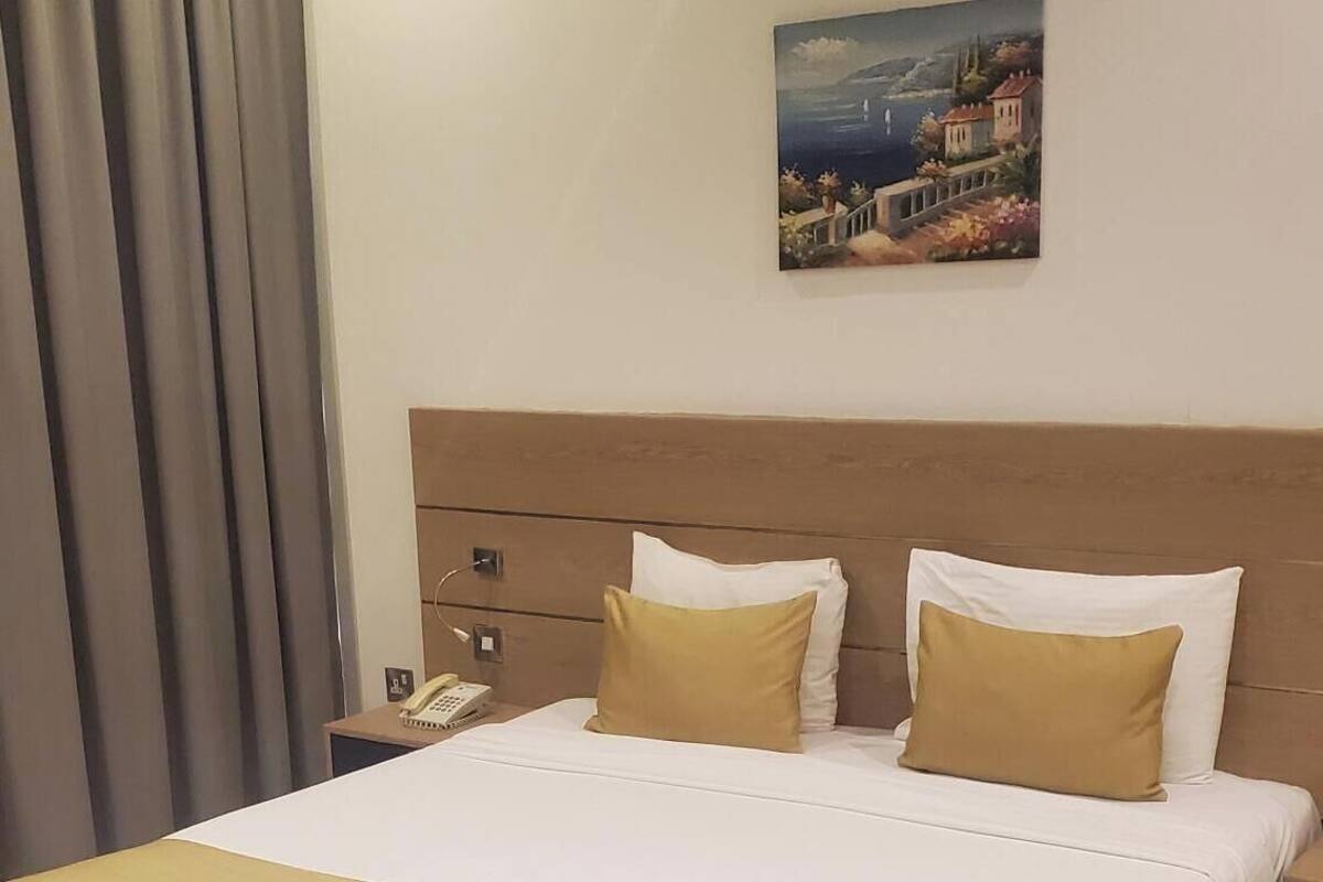 A hotel room with a large bed, a headboard, a bedside table with a lamp, and a painting on the wall.