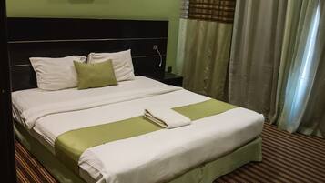 A hotel room with a large bed, a headboard, a painting on the wall, and curtains.