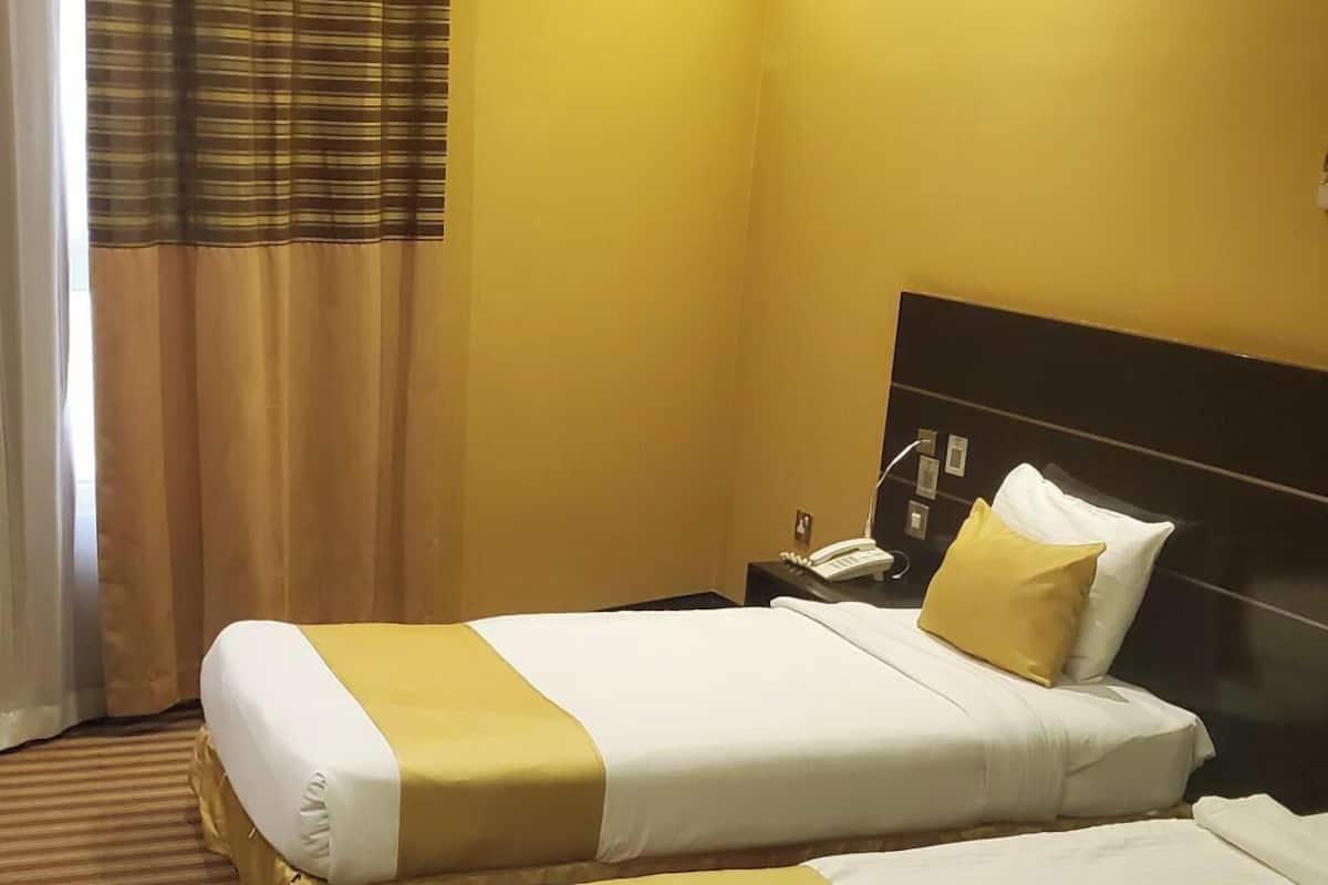 A hotel room with two beds, a nightstand with a phone, and a window with curtains.