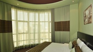 A hotel room with a large bed, a curved ceiling, and a view of the city through large windows. - Al Dar Hotel (Sharjah)
