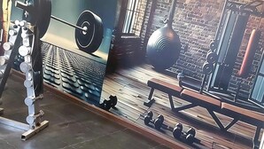 A gym with a mural of a cityscape, weightlifting equipment, and a bench. - Al Dar Hotel (Sharjah)