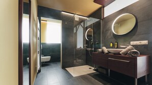 Une salle de bain moderne dotée d’une douche à parois de verre, d’un meuble-lavabo avec un miroir et de toilettes visibles à travers une cloison en verre.