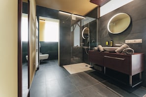 Une salle de bain moderne dotée d’une douche à parois de verre, d’un meuble-lavabo avec un miroir et de toilettes visibles à travers une cloison en verre.