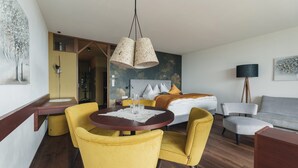 Une chambre d’hôtel avec un lit, une table à manger entourée de chaises jaunes, une lampe et des œuvres d’art accrochées aux murs.