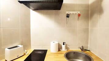 A kitchen with a toaster, a sink, a black induction cooktop, a roll of paper towels, and a soap dispenser.