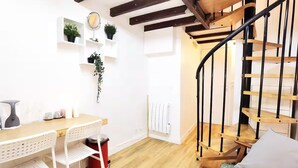 A compact living space with a wooden staircase, white walls, and a small dining area with a table and chairs. - Stylish Marais Duplex near Pompidou & Metro (Paris)