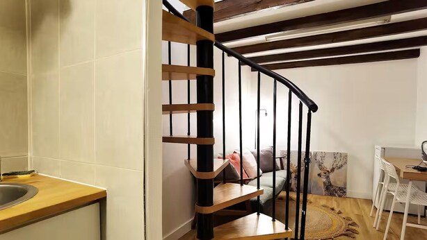 A staircase with wooden steps and black railings, leading to a living area with a sofa, a table, and a rug. - Stylish Marais Duplex near Pompidou & Metro (Paris)