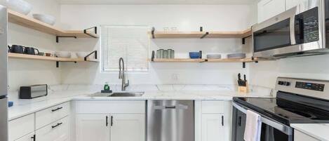 A modern kitchen with white cabinetry, a stainless steel dishwasher, a black oven, and a microwave.
