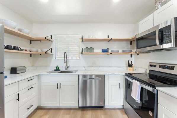 A modern kitchen with white cabinetry, a stainless steel dishwasher, a black oven, and a microwave.