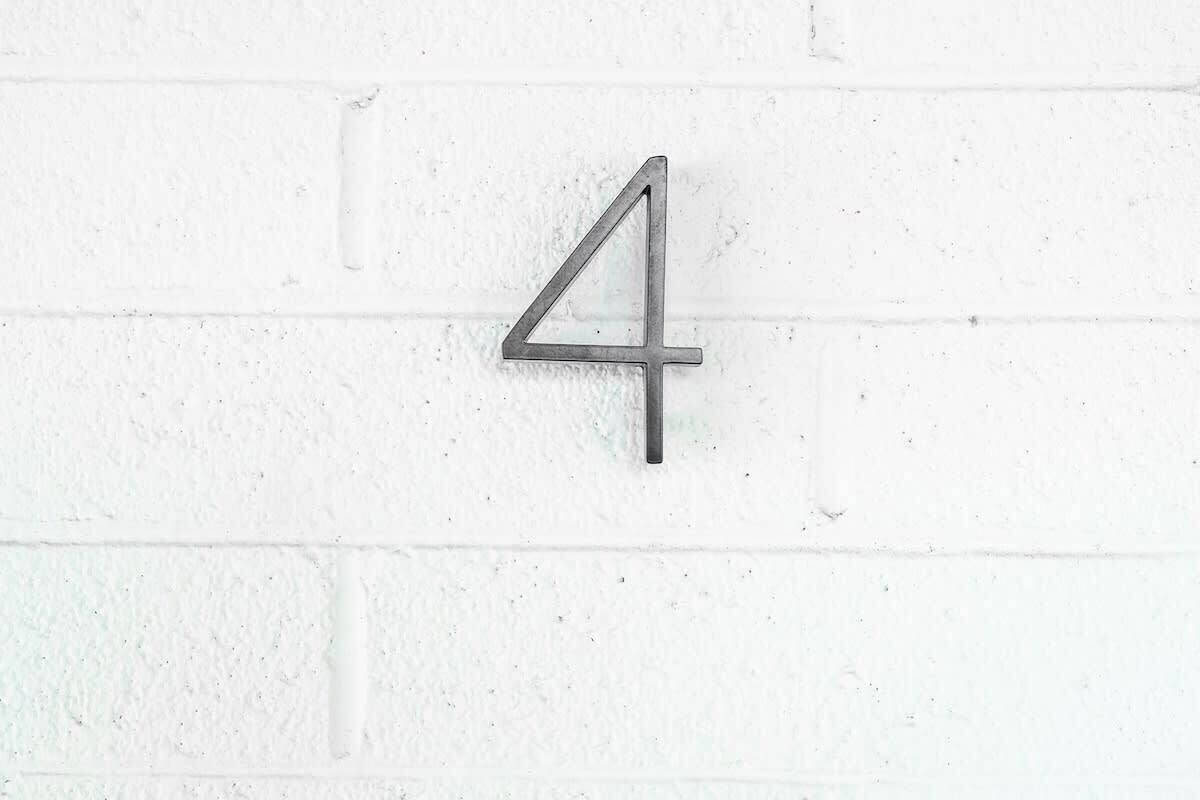 A metal number 4 mounted on a white brick wall.