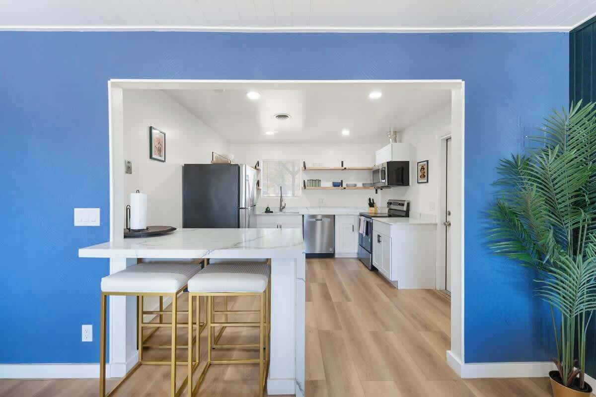 A modern kitchen with white cabinetry, a central island with bar stools, and a potted plant.