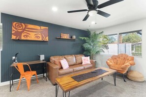 A modern living room with a brown leather sofa, a wooden coffee table, an orange chair, a ceiling fan, and a large plant. - The Rose 4 Apts|Pool|Gazebo|CentralPhx|Sleeps20 (Phoenix)