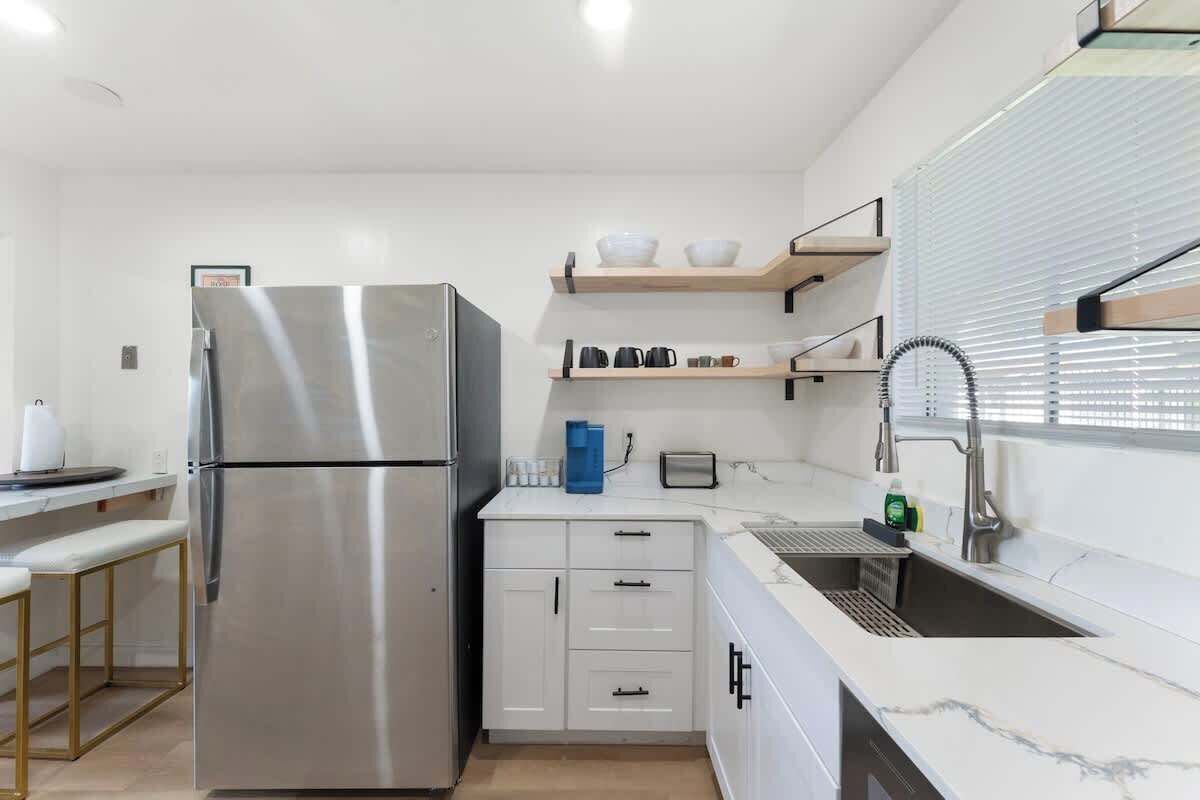 A modern kitchen with a stainless steel refrigerator, white cabinetry, and a built-in sink.