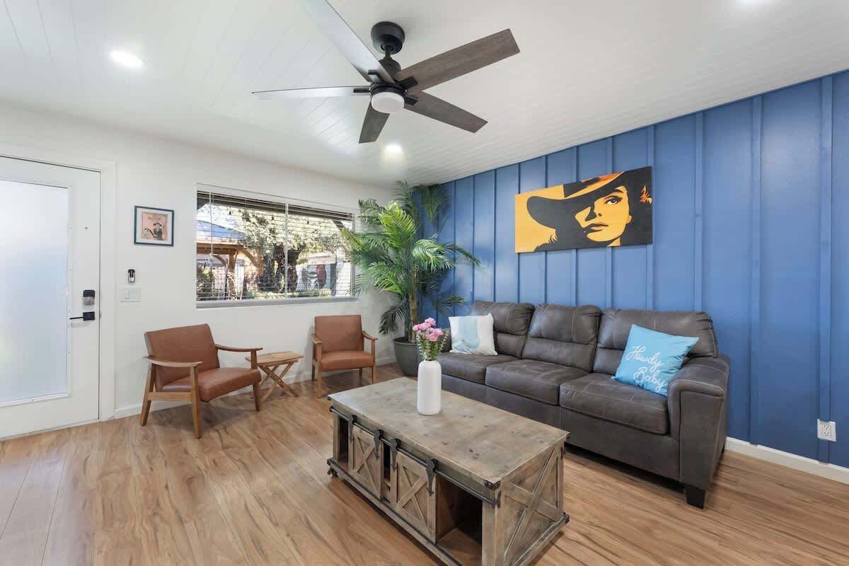 Un salon avec un mur d’accent bleu, un canapé en cuir marron, une table basse en bois et un ventilateur de plafond.