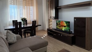 Una sala moderna con comedor, un sofá, un televisor sobre un mueble de madera y una ventana con cortinas traslúcidas.