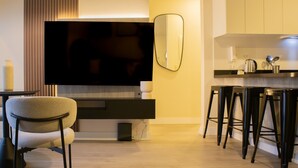 A modern kitchen with a large flat-screen TV, a bar stool area, and a dining table with chairs.