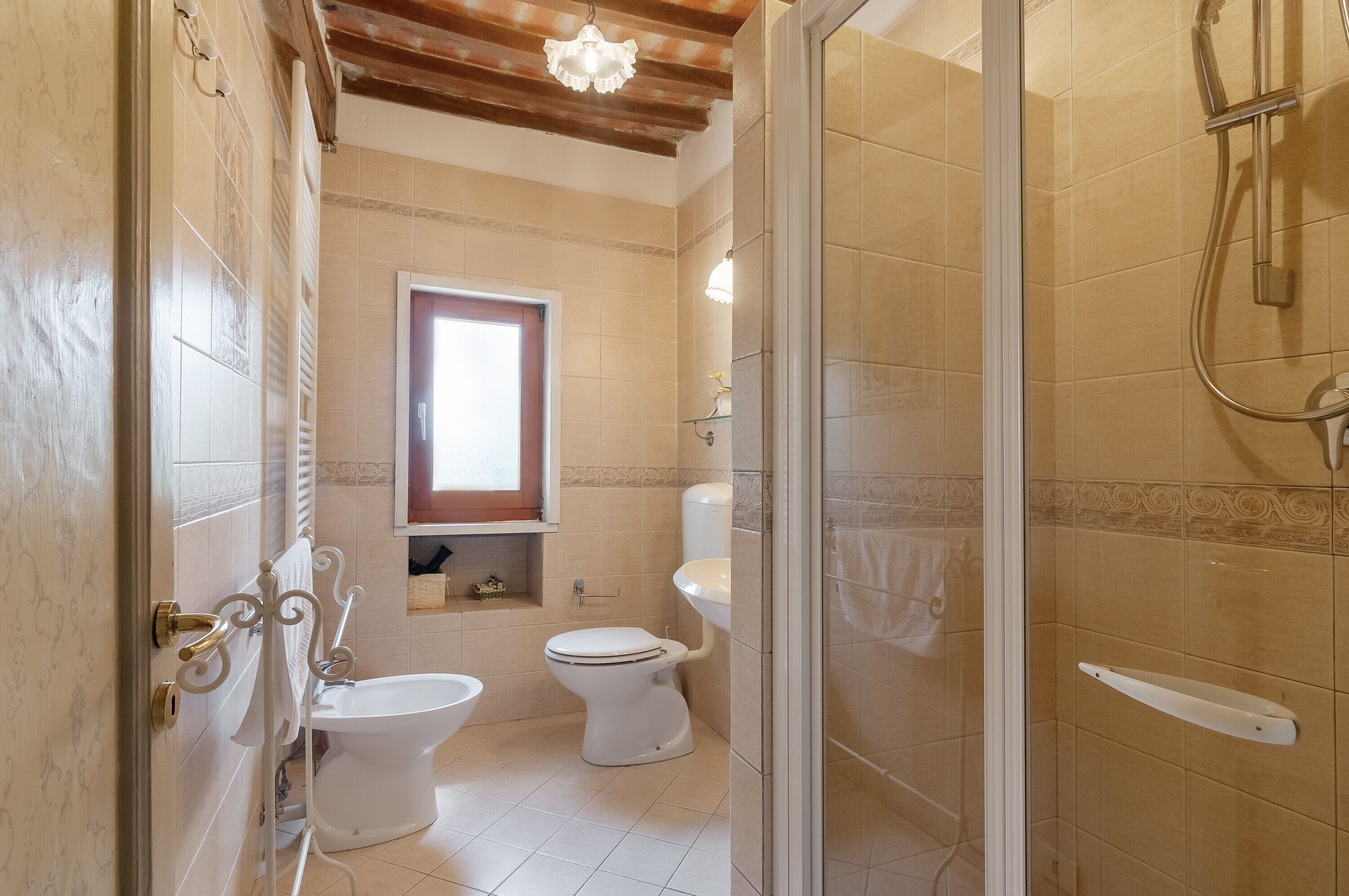 Ein Badezimmer mit Toilette, Bidet und Duschbereich, mit einem Fenster für natürliches Licht.