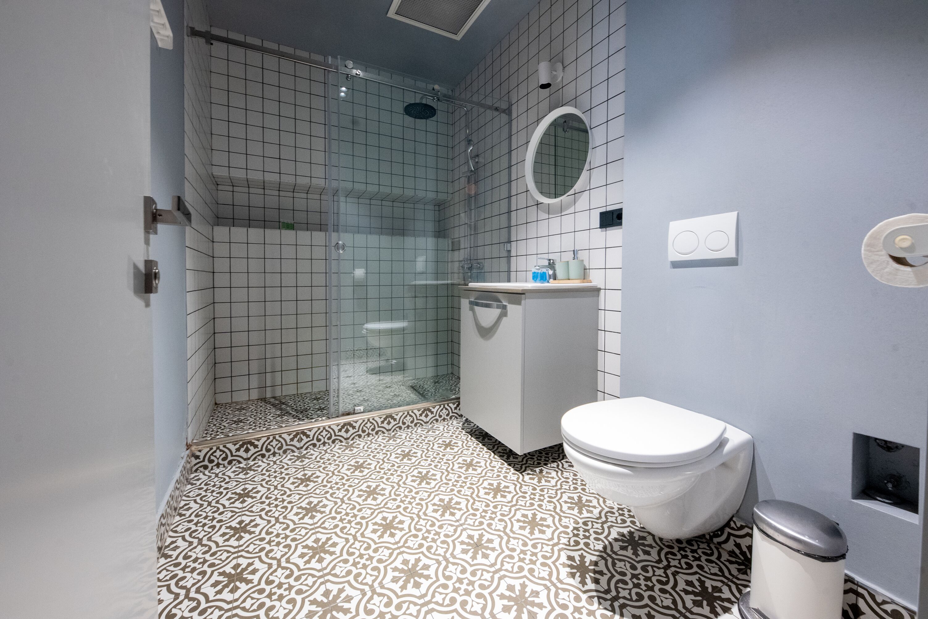 Ein Badezimmer mit einem gemusterten Boden, einer Toilette, einem Waschbecken und einer Duschkabine.