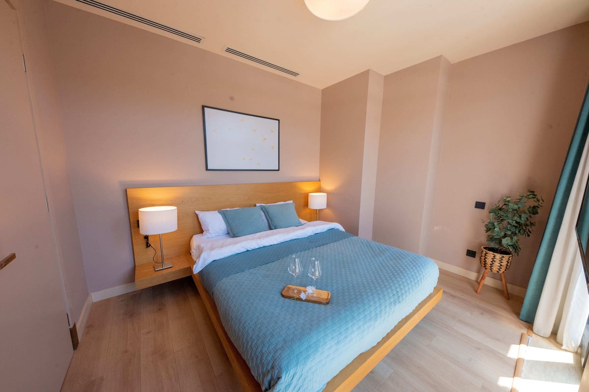 A neatly made bed with a blue bedspread, two bedside lamps, and a framed picture on the wall.