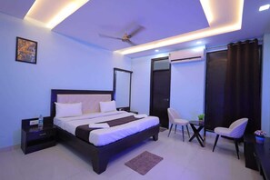 A modern bedroom with a large bed, bedside tables, a ceiling fan, and a seating area with chairs. - Shakti villa home stay (Agra)