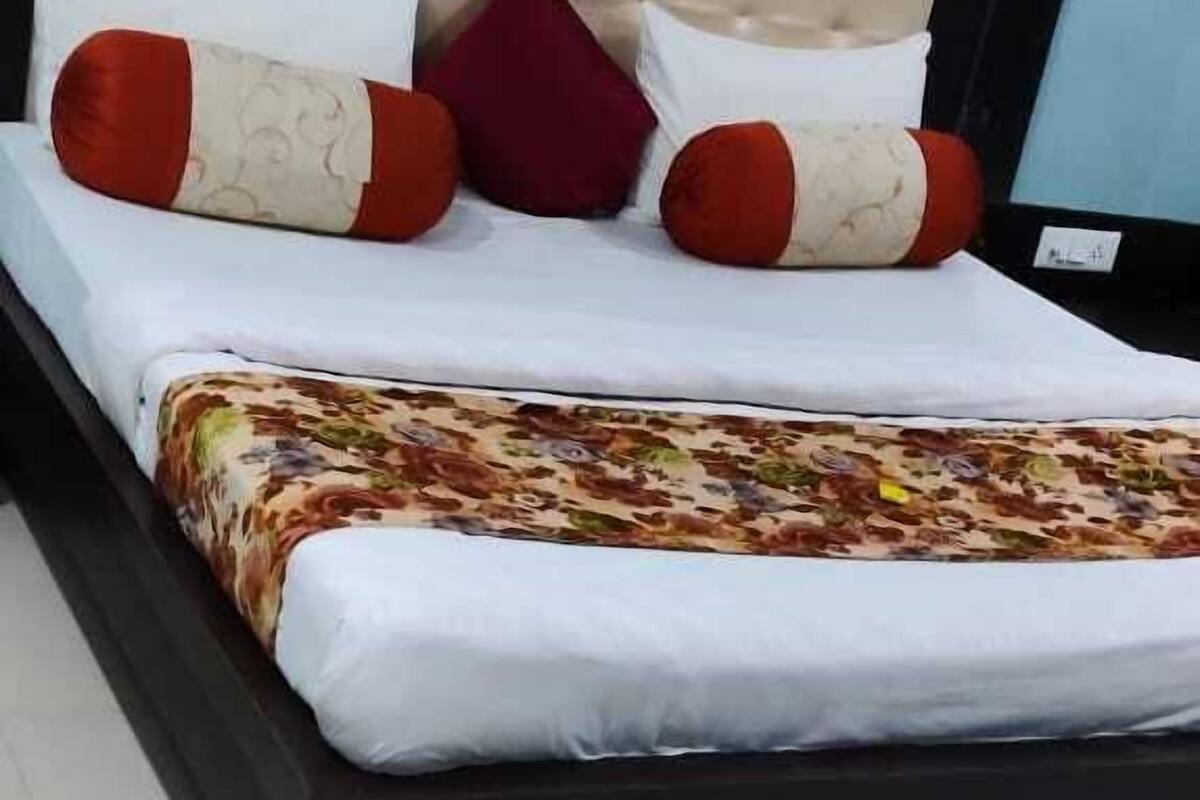 A bed with a floral-patterned bedspread, a headboard, and multiple pillows in red and white.
