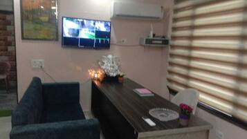 A living room with a dark wooden coffee table, a blue sofa, and a flat-screen TV mounted on the wall.