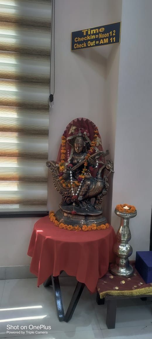 Una estatua sobre un paño rojo, un cartel con detalles horarios y un pequeño altar con flores.