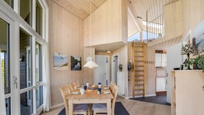 Un vaste espace de salle à manger avec une table et des chaises en bois, une moquette bleue et une vue sur la cuisine et l’étage supérieur.