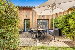 A wooden deck with a table and chairs, a large umbrella, and a sofa.