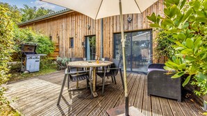 A wooden deck with a round table and chairs, a grill, and a covered seating area.