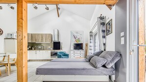 A bedroom with a bed, a desk, a chair, a kitchenette, and a bathroom.